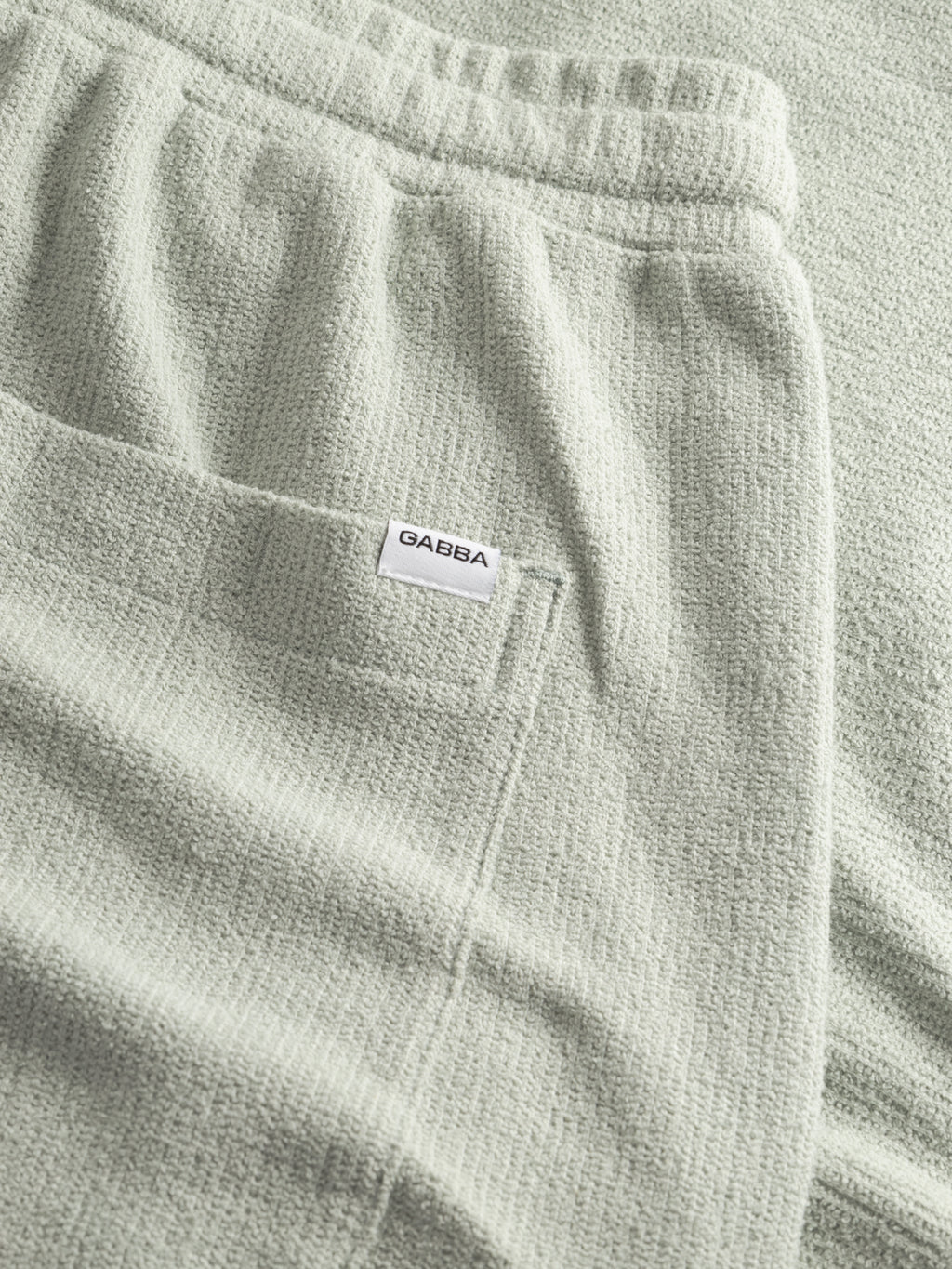 Close-up of GABtommi Towel Shorts in Mineral Gray by Gabba, featuring textured terry cotton, an elastic waistband, and a pocket with a small white Gabba label.