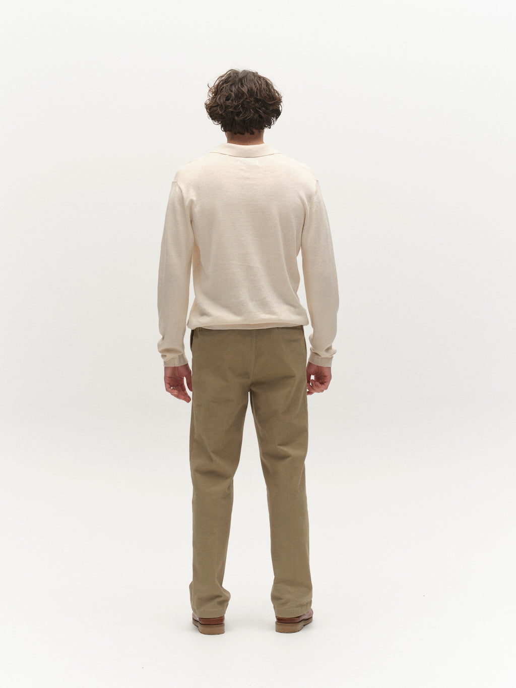 A person with short, curly hair faces away from the camera, wearing the Gabba GABcross Dush LS Knit in Sand Mel., khaki pants, and brown shoes against a plain white background.