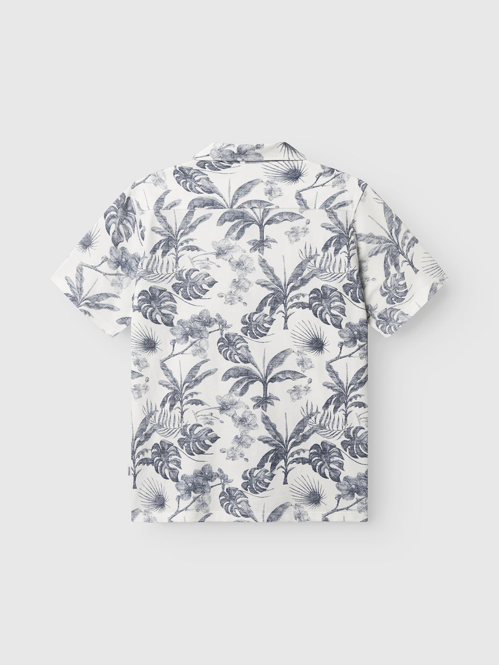 The Gabba GABsven Reg Leaves SS Shirt - Flower Mix is a short-sleeved white piqué jersey shirt with a blue tropical leaves-and-flowers print, shown flat with the back facing up on a plain light background.