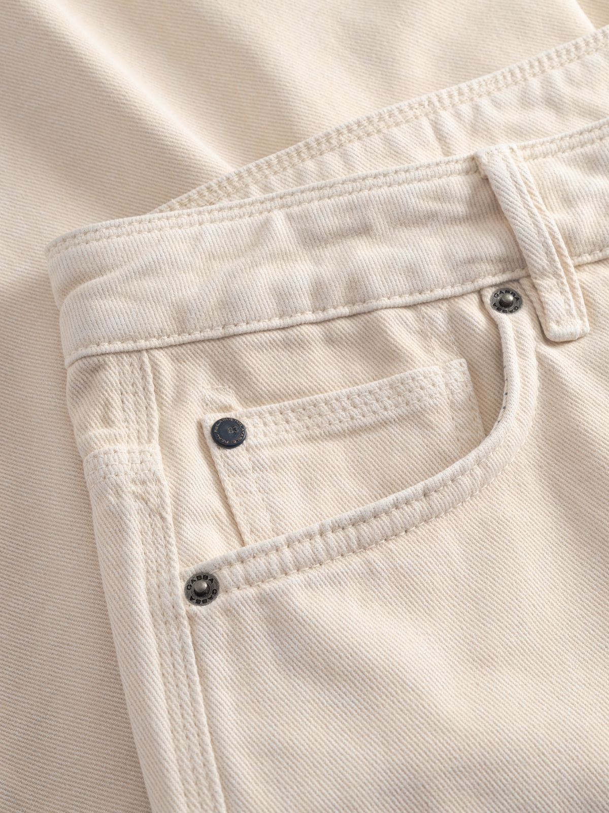 Close-up of the front pocket and waistband of Gabba GABmox Antiq Shorts in ecru, showing stitching details, a coin pocket, and metal rivets on rigid twill with a garment-dyed antique finish.