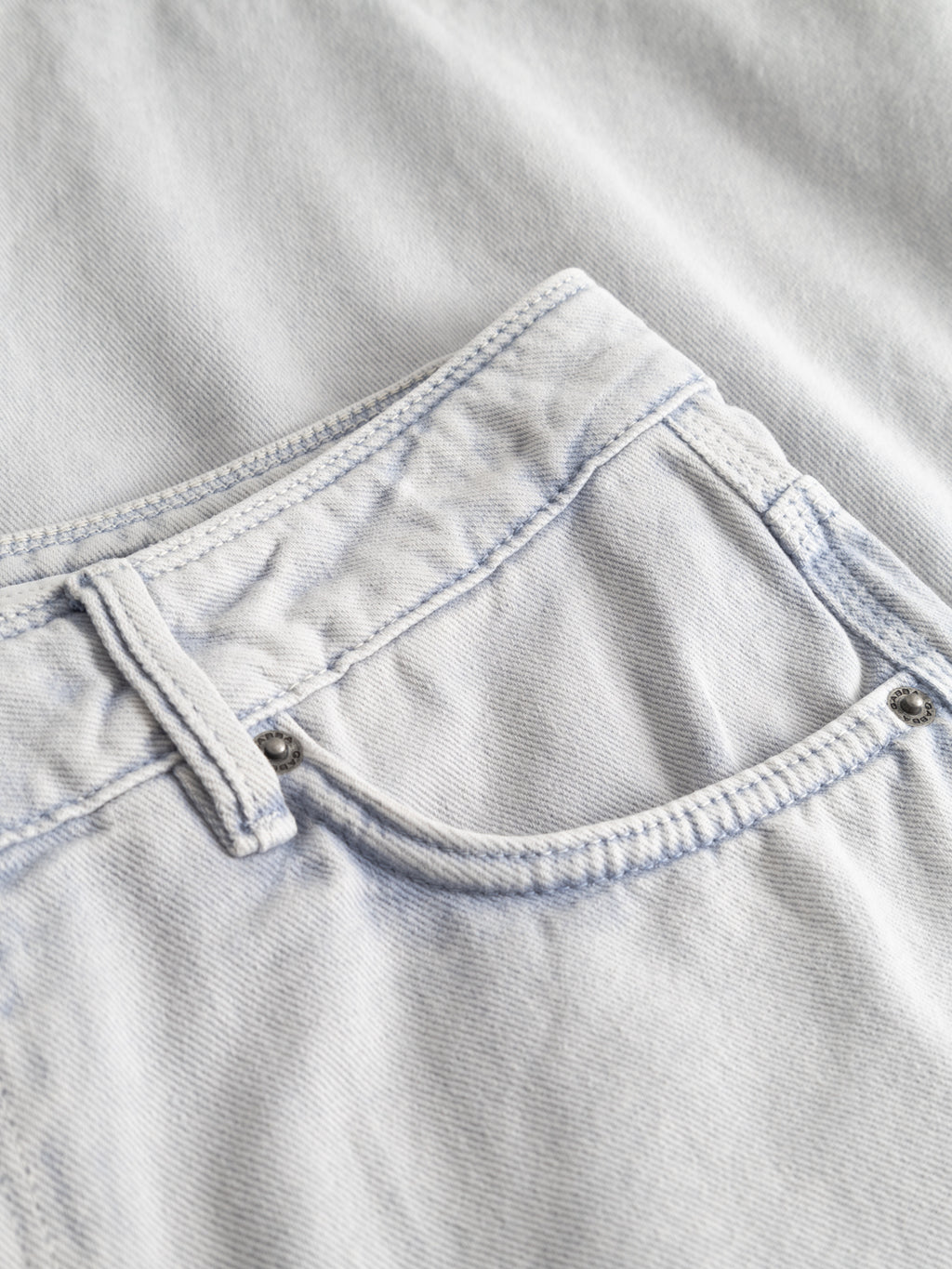 Close-up of the GABmox Antiq Shorts - Denim Blue by Gabba, featuring light-wash denim with visible stitching, a belt loop, and metal rivets on rigid twill fabric finished with an antique garment-dyed look.
