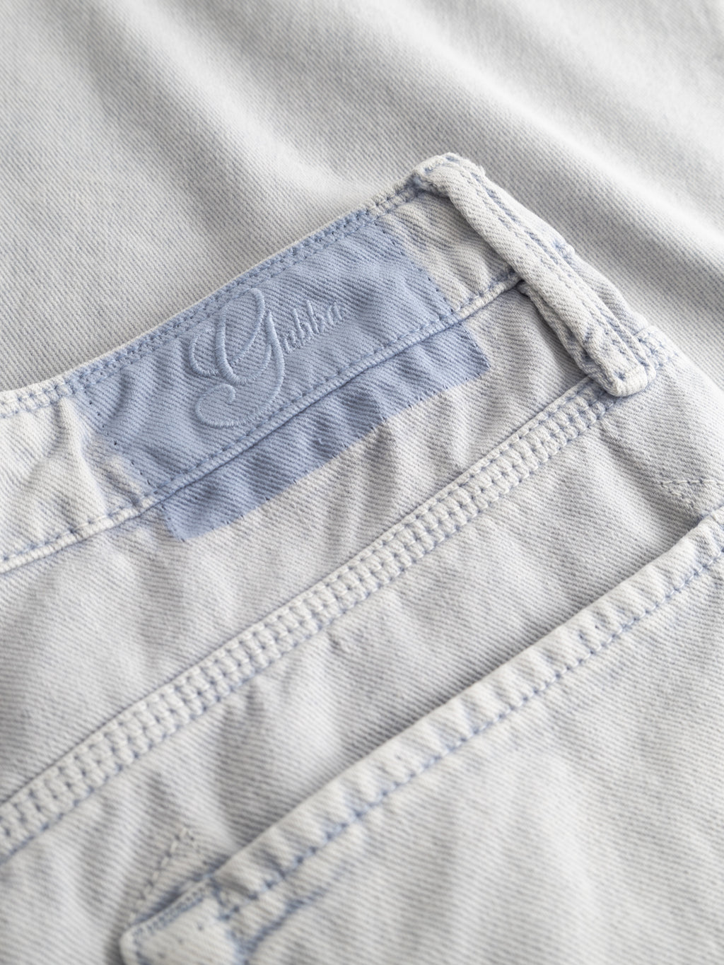 Close-up of Gabba GABmox Antiq Shorts in denim blue, highlighting the waistband, belt loops, fabric label with cursive script, visible stitching, and textured rigid twill.