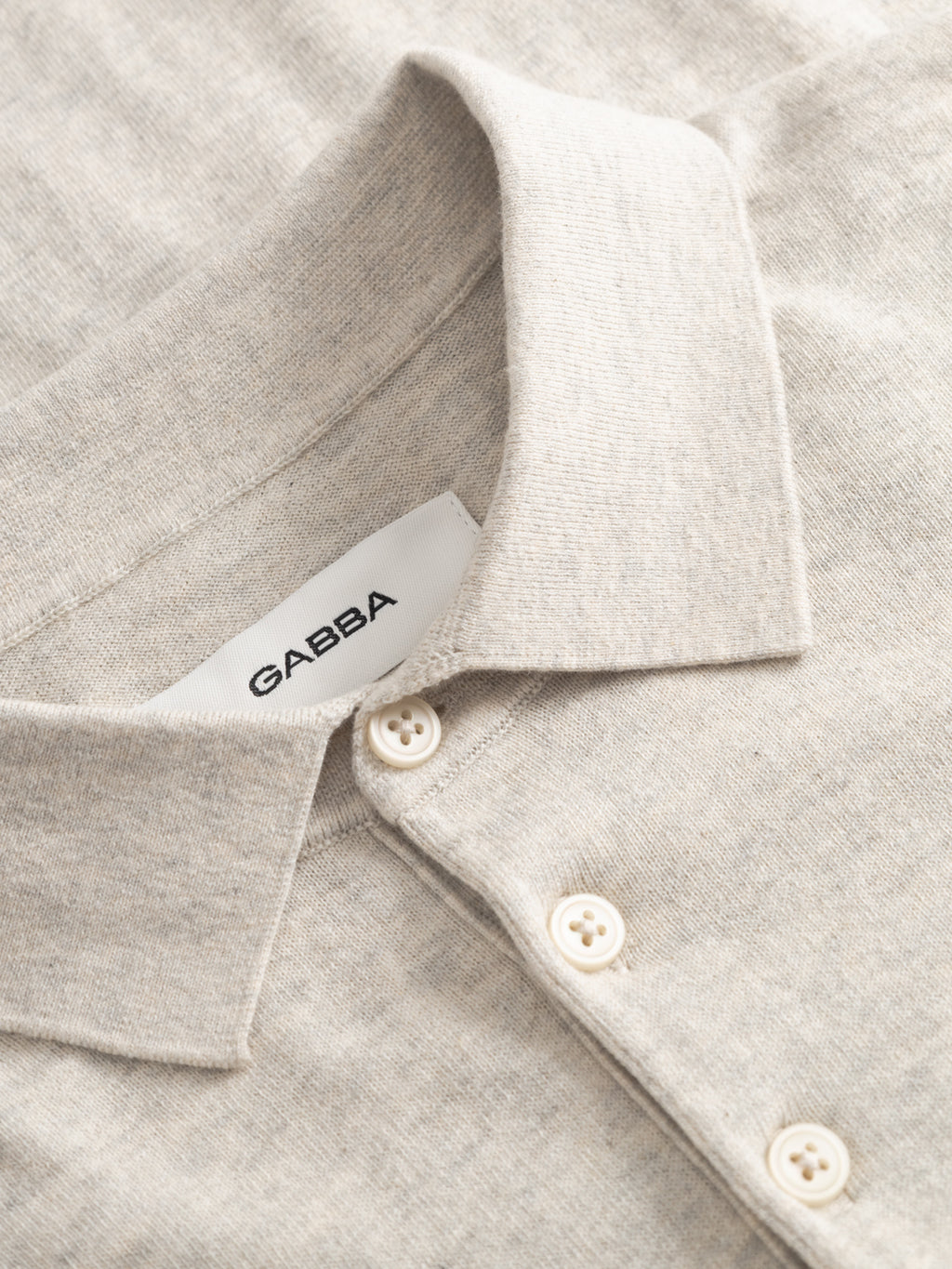 Close-up of a Gabba GABbenson New Cot SS Knit men's regular fit polo in Sand Mel, highlighting the collar, white brand label, and cream buttons on the placket.