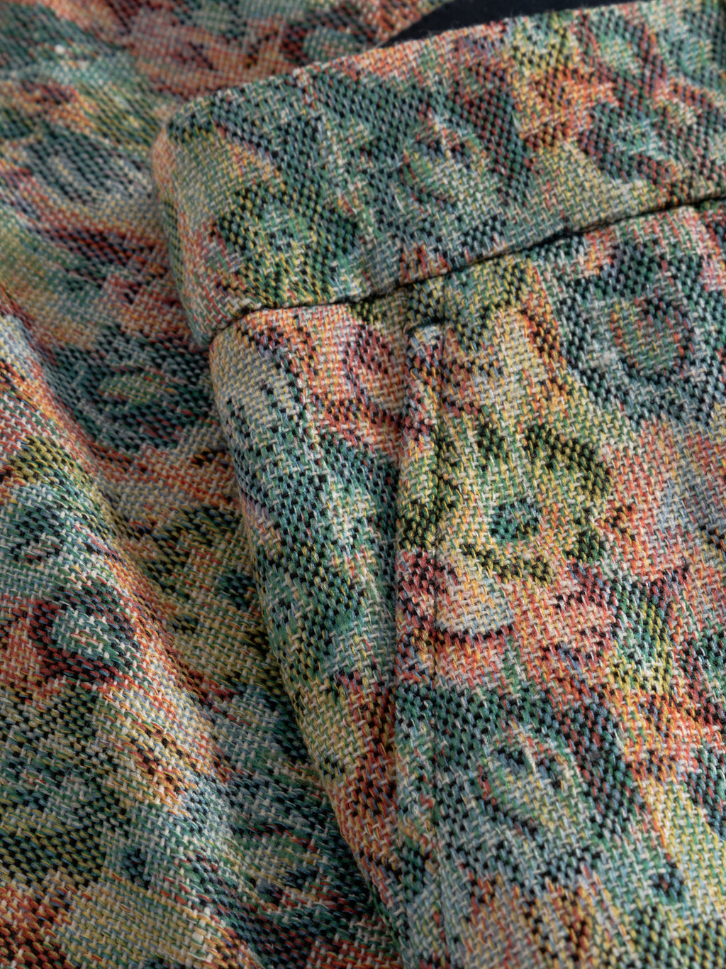 Close-up of Gabba's GABjoli Ted Kscope Shorts - Abstract Flowers, showing a folded edge and visible stitching on multicolored fabric with an abstract floral pattern in green, yellow, pink, and orange—ideal for versatile seasonal style.