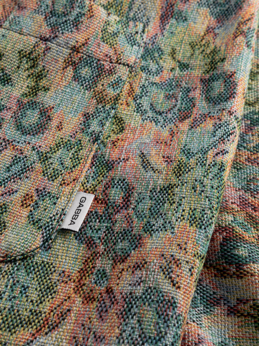 Close-up of the GABjoli Ted Kscope Shorts - Abstract Flowers by Gabba, featuring textured fabric with intricate green, yellow, and pink woven patterns. A small white label with 