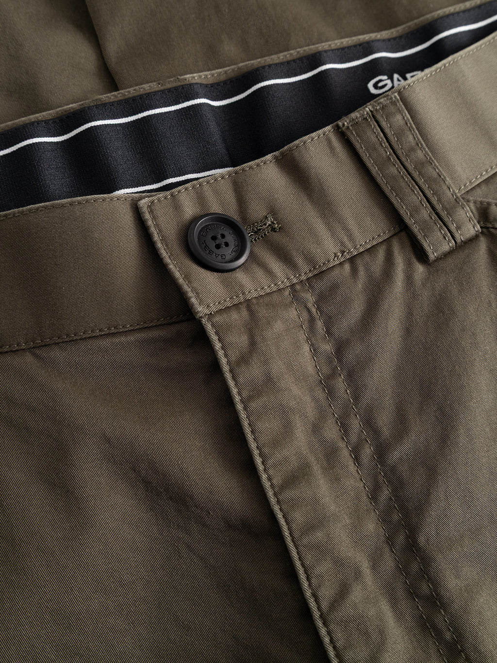 Close-up of the Gabba GABjoe Vico Cargo Pant - Army, featuring an olive green waistband, black button, visible stitching, and a glimpse of the striped inner lining.