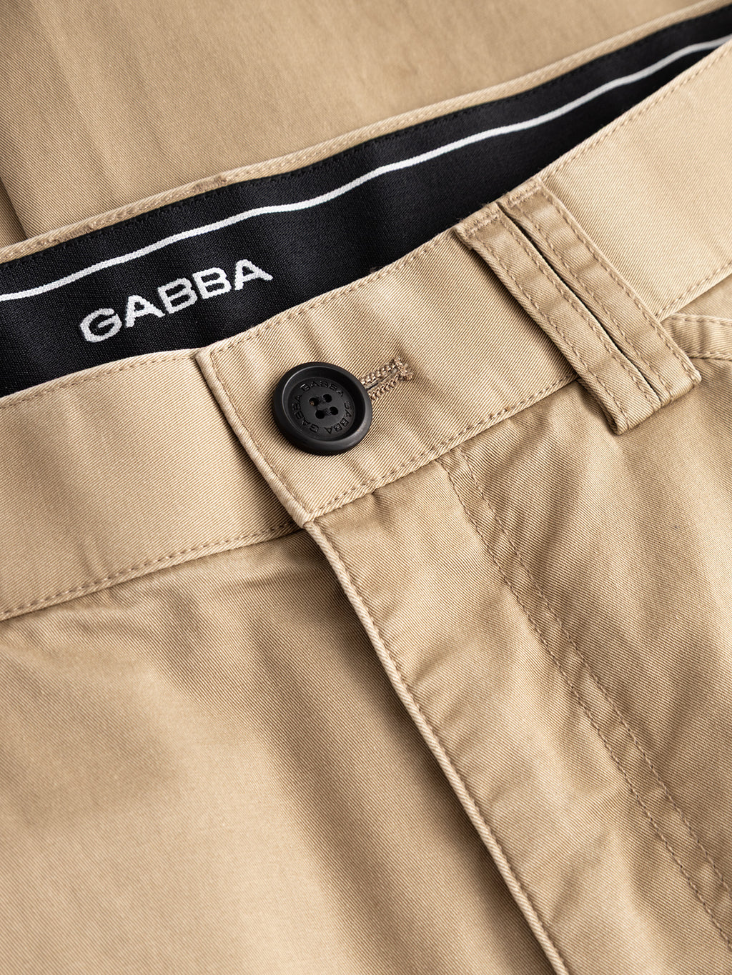 Close-up of the Gabba GABjoe Vico Cargo Pant in sand, featuring beige utilitarian design, black button, visible stitching, and an inner waistband with a black strip bearing the white Gabba logo.