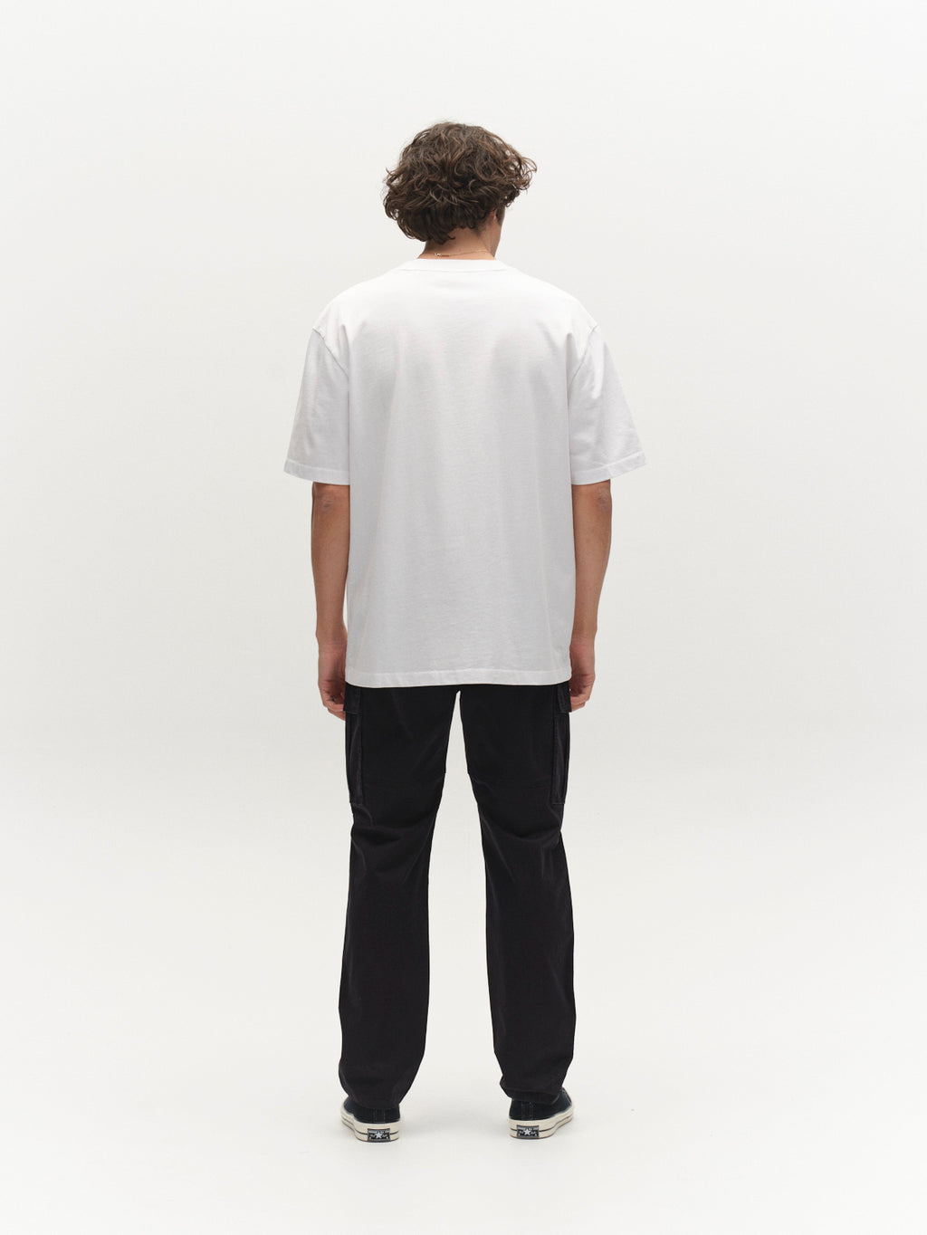 A person with short curly hair stands facing away, wearing a plain white t-shirt, sneakers, and Gabba's GABjoe Vico Cargo Pant in black against a plain white background.