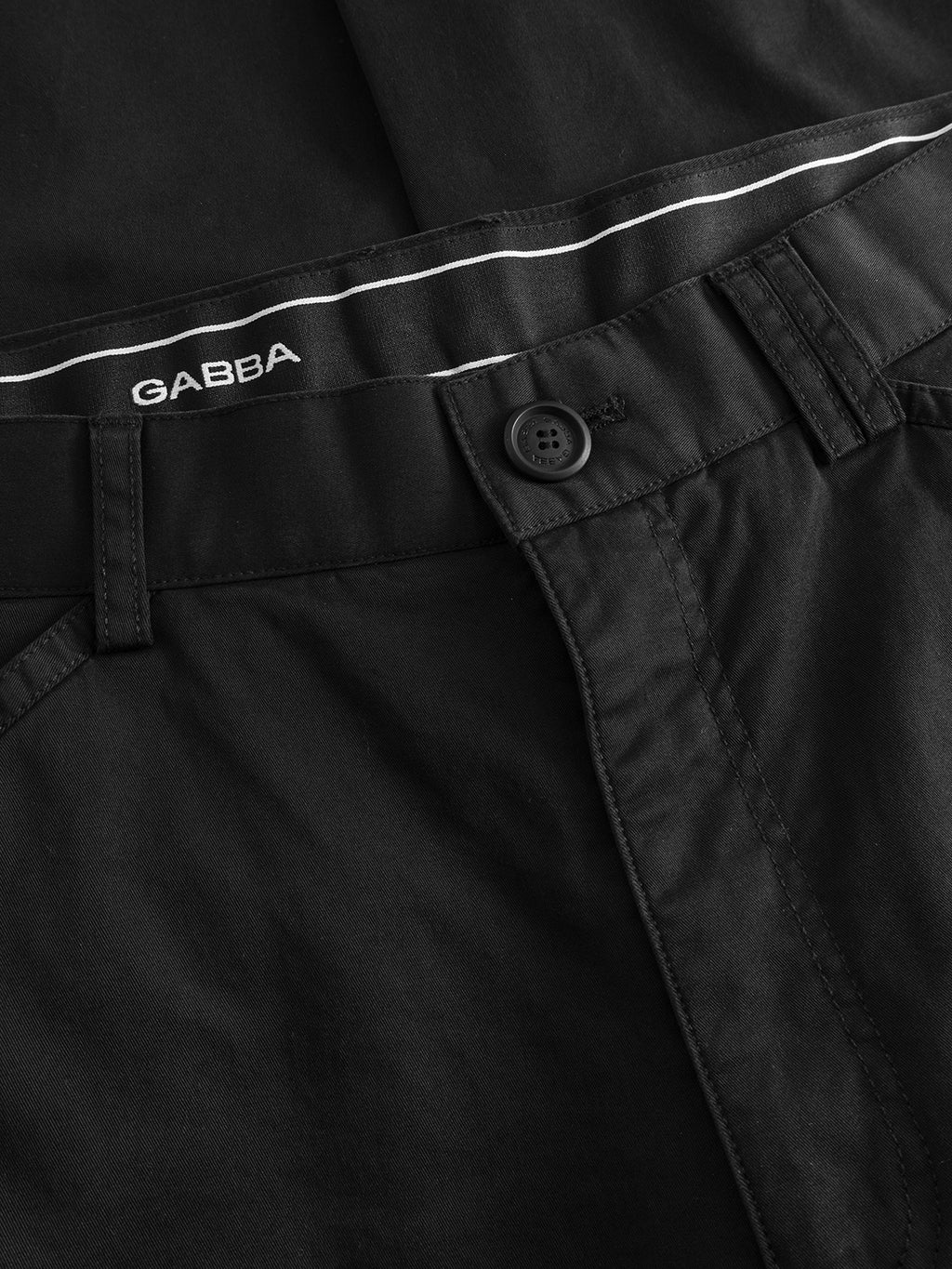 Close-up of the waistband and front of GABjoe Vico Cargo Pant in black by Gabba, featuring a button, belt loops, white piping, and the Gabba logo on the inside waistband.
