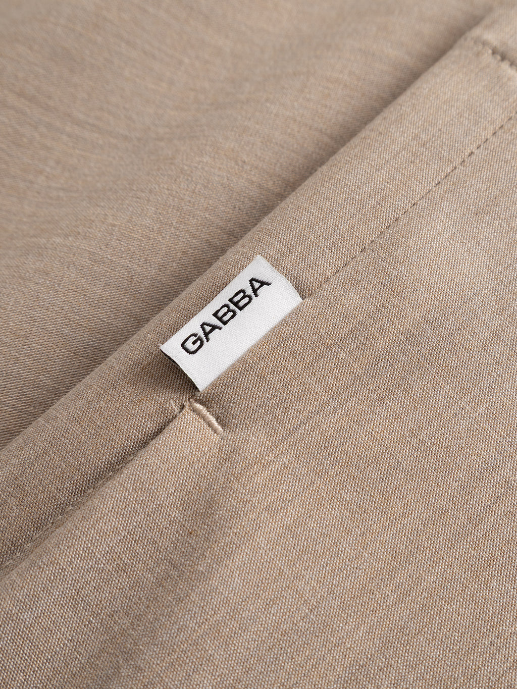 Close-up of the GABtogger Tailor Dressy Overshirt in sand by Gabba, showcasing its refined beige fabric and a white “GABBA” tag sewn into the seam, possibly near a pocket.