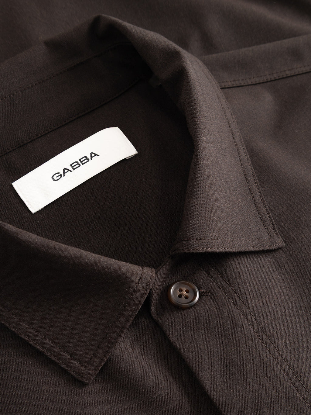 Close-up of the Gabba GABtogger Tailor Dressy Overshirt in black, featuring a button and a white Gabba label inside the collar. The smooth fabric and detailed stitching make it ideal for smart layering or as a dressy overshirt.
