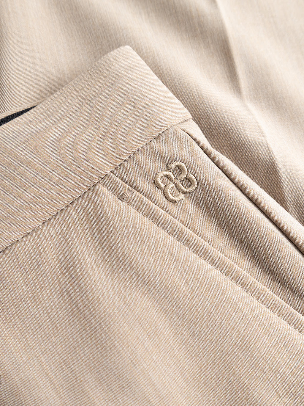 Close-up of Gabba’s GABjoe Tailor Dressy Pant in sand, showing a subtle embroidered double “B” logo near the pocket and emphasizing the textured fabric and fine stitching for a refined, tailored finish.