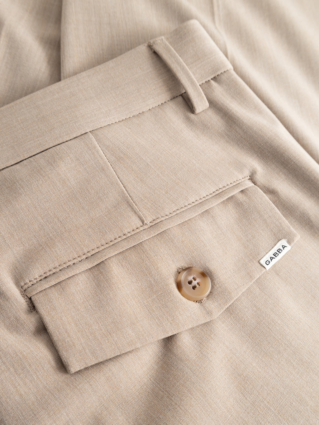 Close-up of the GABjoe Tailor Dressy Pant in Sand by Gabba, highlighting the back pocket with button closure and a small white Gabba label on the seam. The fabric appears smooth with a subtle texture.