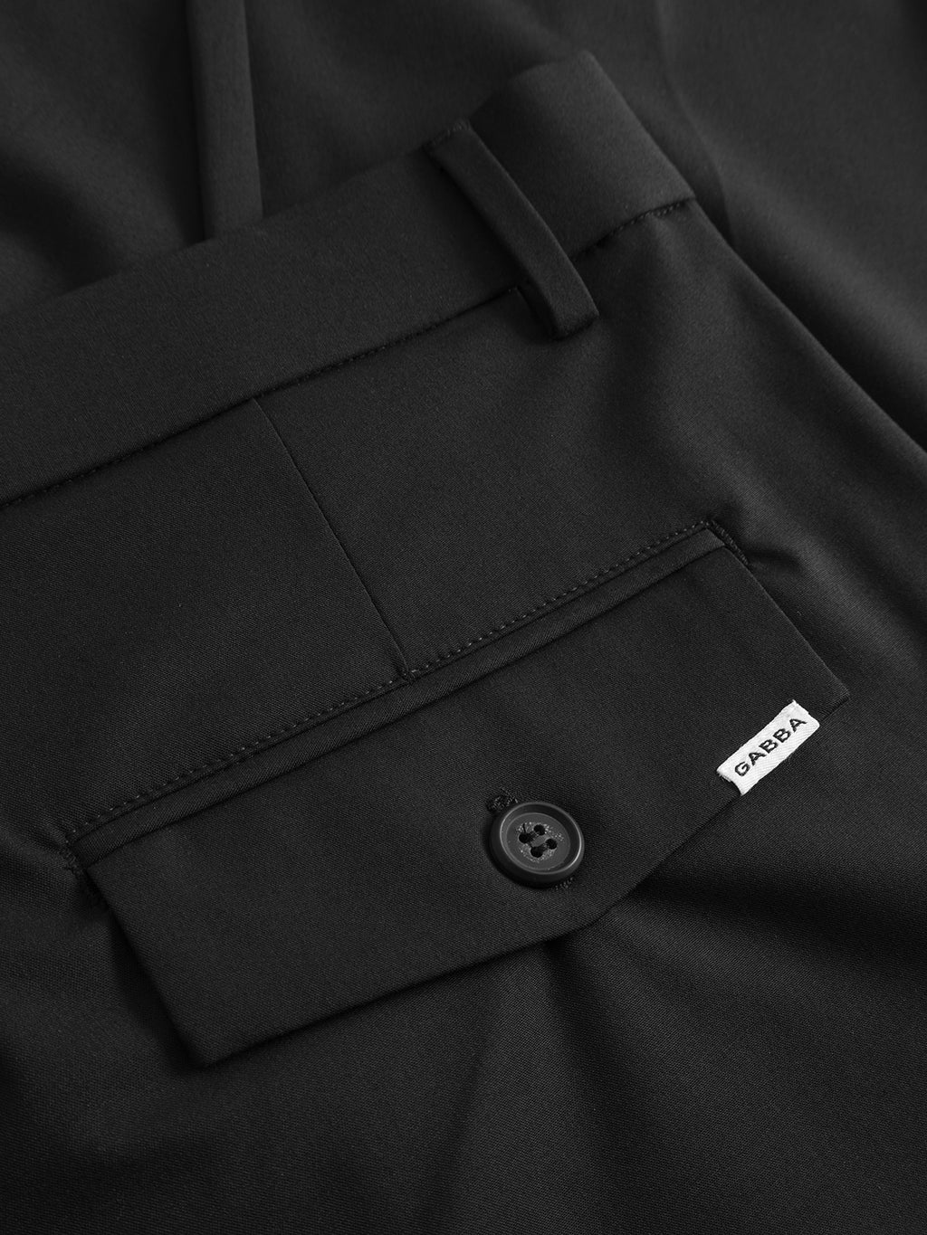 Close-up of the back pocket on the GABjoe Tailor Dressy Pant in black by Gabba, showing a buttoned flap and a small white GARPA label sewn on the pocket edge.