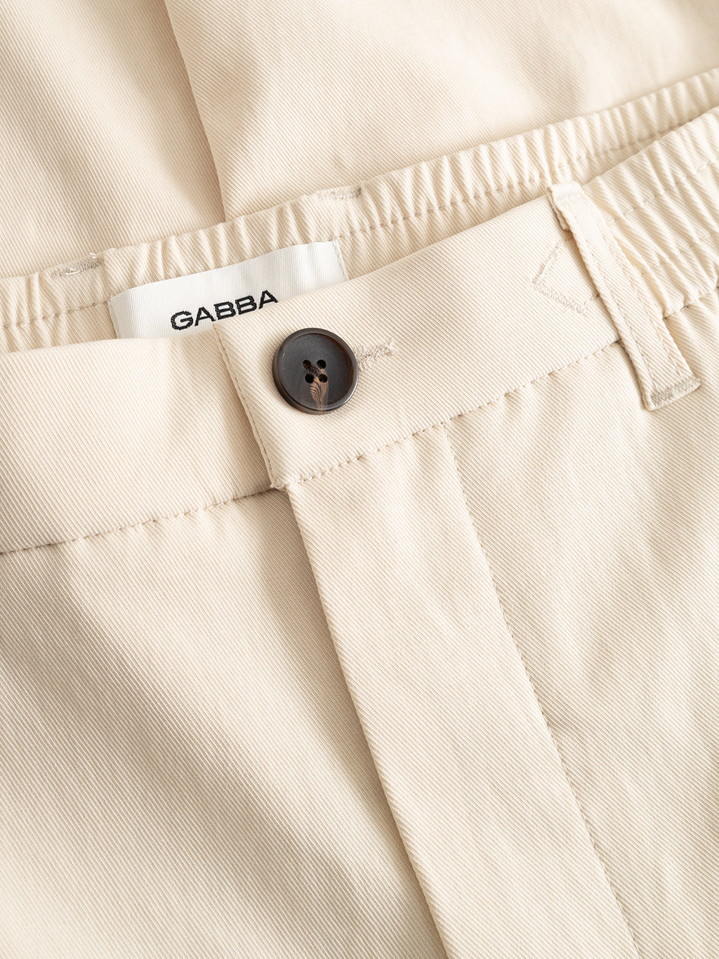 Close-up of Gabba GABmonza Tasca Bolu TENCEL™ Pant in Birch, featuring a black button, belt loop, and a white GABBA label. The soft, slightly textured fabric and relaxed straight fit provide comfort and style.