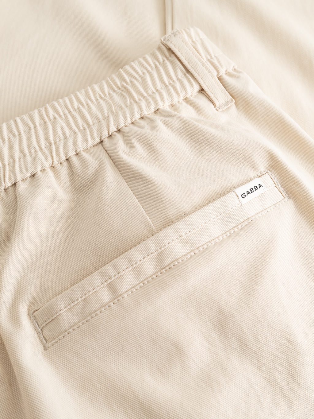 Close-up of the GABmonza Tasca Bolu TENCEL™ Pant in Birch by Gabba, featuring an elastic waistband, single welt pocket with a white Gabba label above it, and a relaxed straight fit for comfort and effortless style.
