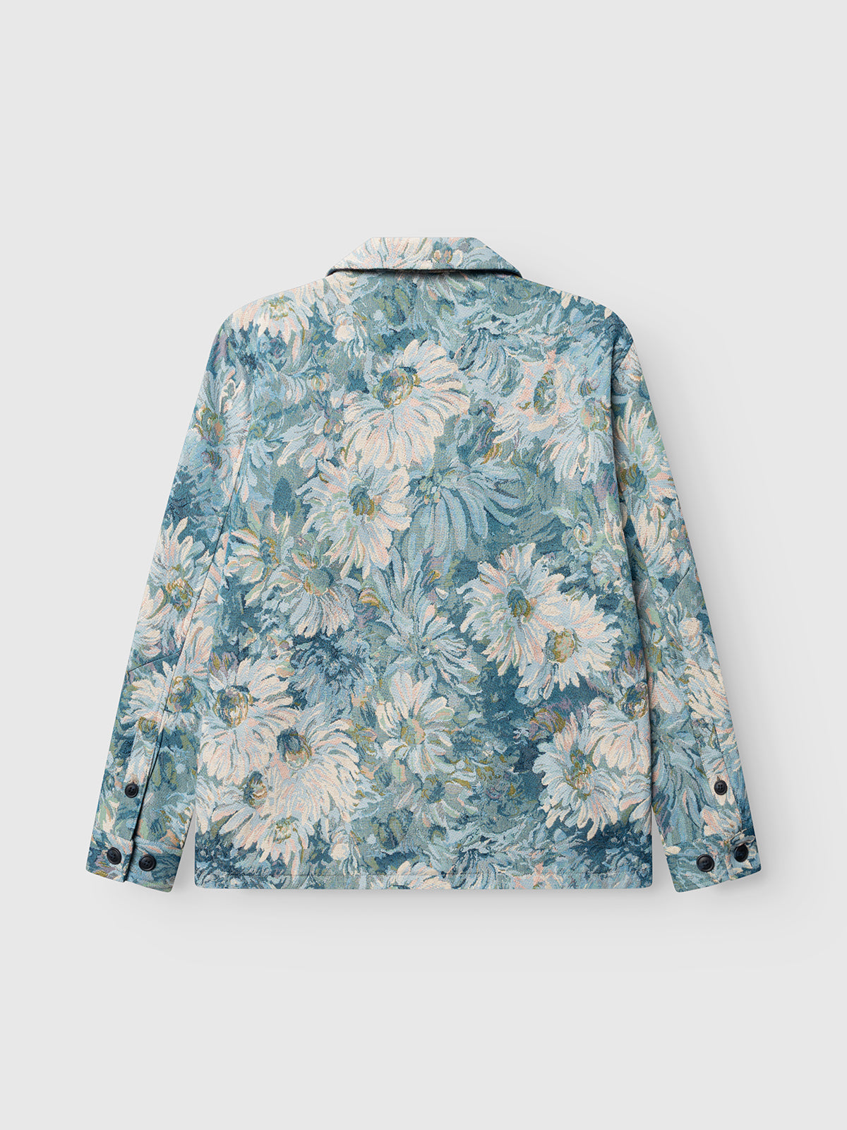 The Gabba GABsimone Art LS - Blue Pattern overshirt features an all-over floral print with large white and pale yellow flowers and green leaves on a light blue background, shown from the back, and has black buttons on the cuffs.