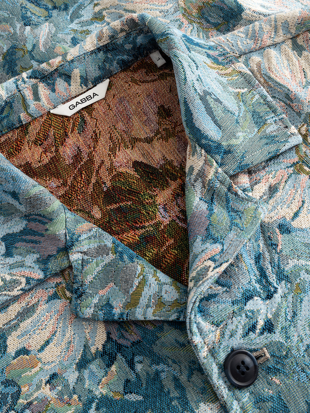 Close-up of the Gabba GABsimone Art LS - Blue Pattern overshirt, featuring a blue and green floral print, visible collar and button details, branded label, and an inner lining with a contrasting earthy floral design.
