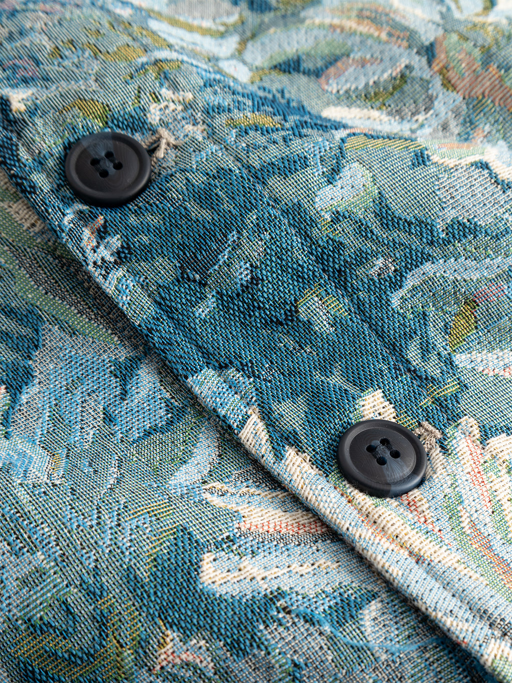 Close-up of Gabba's GABsimone Art LS - Blue Pattern overshirt, showcasing its textured, tapestry-like blue and green abstract fabric with two black buttons.