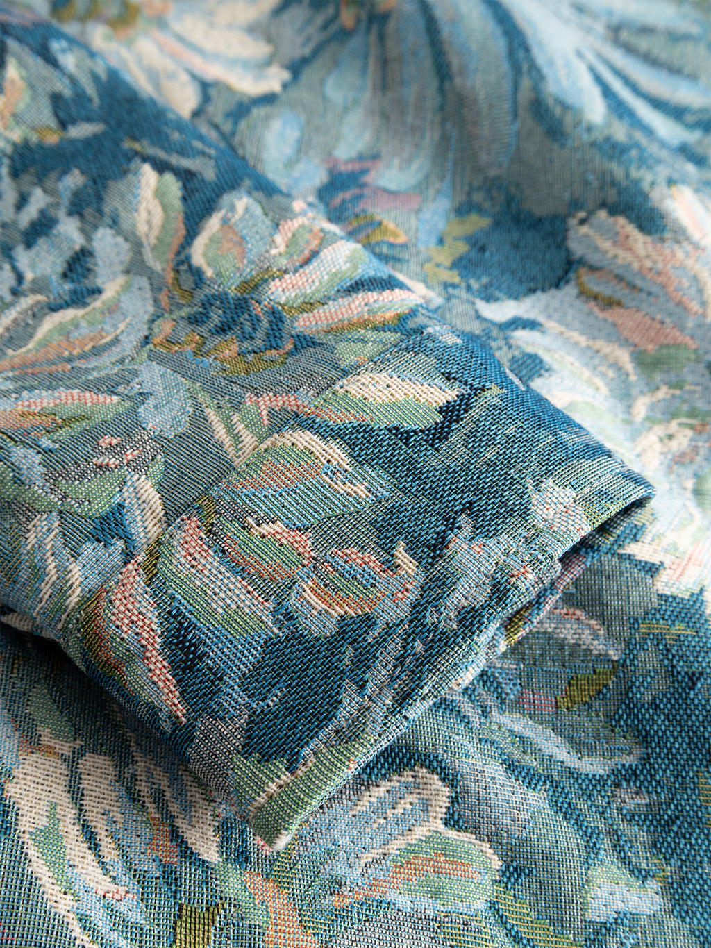 A close-up of the GABsimone Art LS - Blue Pattern by Gabba shows its sleeve crafted from blue and pastel floral tapestry fabric, highlighting the brocade's intricate woven textures and patterns.