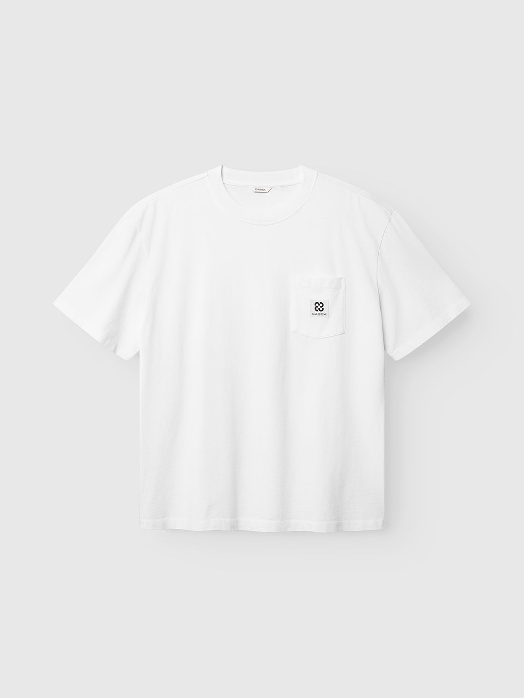 The Gabba GABnigel Wix Pkt Boxy Hour SS T-Shirt in white features a boxy fit, short sleeves, a small chest pocket with a black geometric logo, and is made from heavyweight cotton. Displayed against a light gray background.
