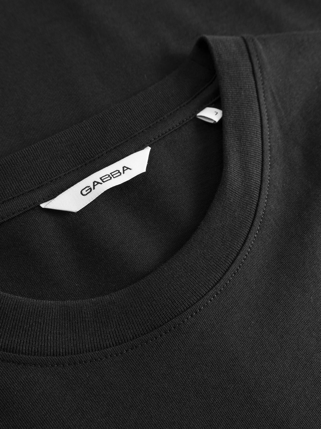 Close-up of a black GABdune Element GOTS SS T-Shirt by Gabba, classic fit with crew neck and white Gabba label inside the collar. The soft organic cotton fabric appears neatly stitched and comfortable.