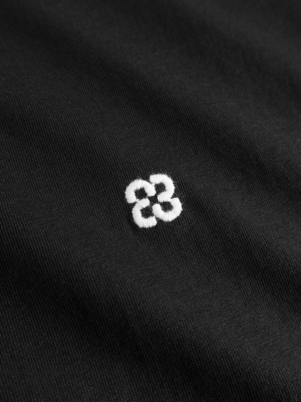A close-up of the Gabba GABdune Element GOTS SS T-Shirt in black reveals organic cotton fabric with a small white embroidered design of two interlocking circles or an 