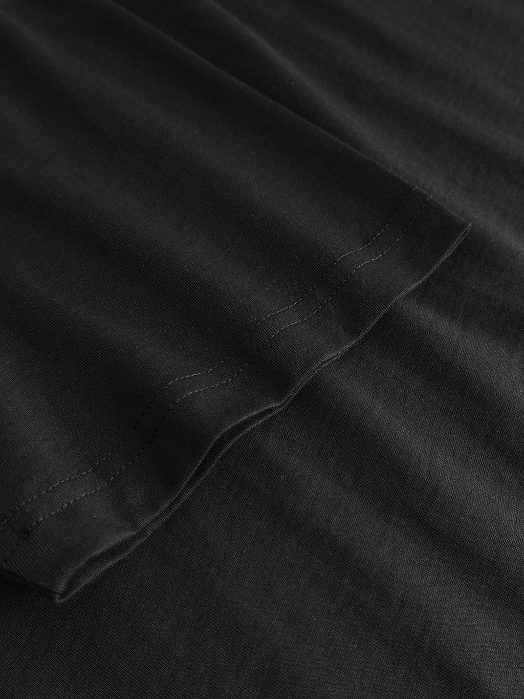 Close-up of the hem of the black Gabba GABdune Element GOTS SS T-Shirt, highlighting its neat stitching and smooth organic cotton fabric texture against a black surface.