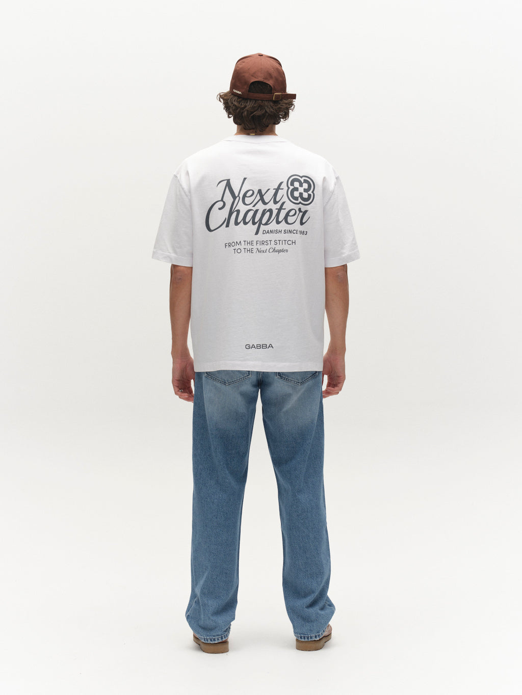 A man wears the Gabba GABlegin Wix Chap Boxy Hour SS T-Shirt in white, made from heavyweight cotton with “Next Chapter” and a bold back graphic, while standing in a plain studio setting.