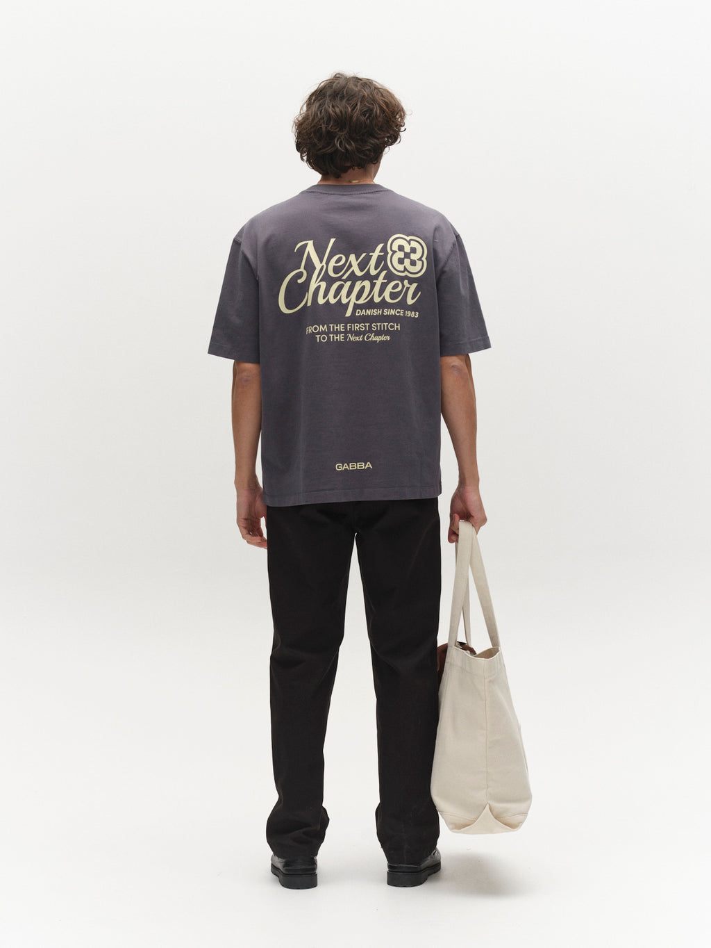 A person with short, curly hair faces away, wearing the Gabba GABlegin Wix Chap Boxy Hour SS T-Shirt in Turbulence Blue with a 