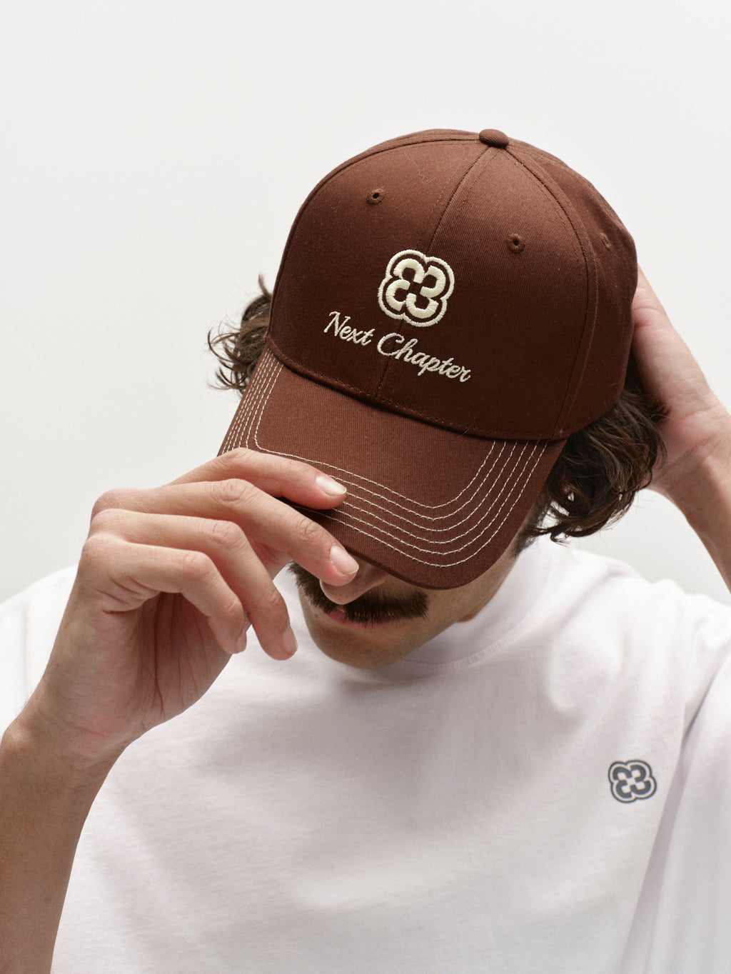 A person tilts the Gabba GABchap Cap - Brown Choco, featuring 