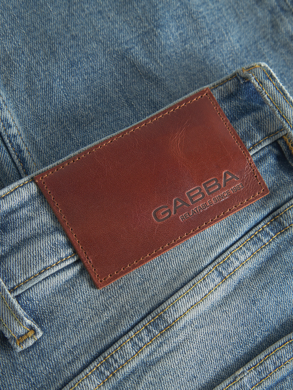 Close-up of GABalex Cros Cropped Lt. Blue Denim jeans by Gabba, made from recycled cotton. A brown leather patch above the back pocket is embossed with 