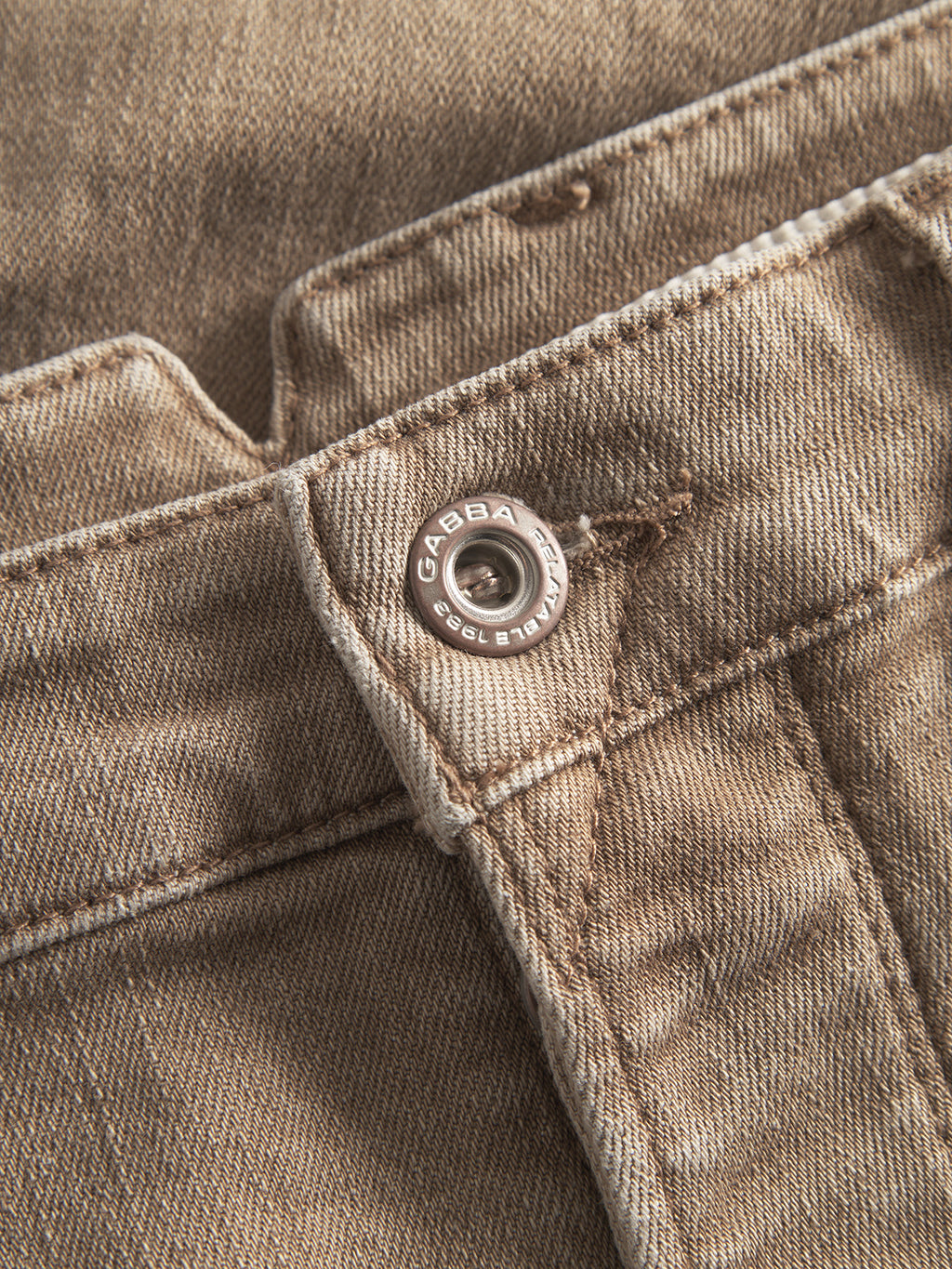 Close-up of GABalex Earth - Sand jeans by Gabba, featuring a metal button engraved with GABBA and EST. 1983. The relaxed-fit denim's sand tone, stitching, and fabric texture are clearly visible.
