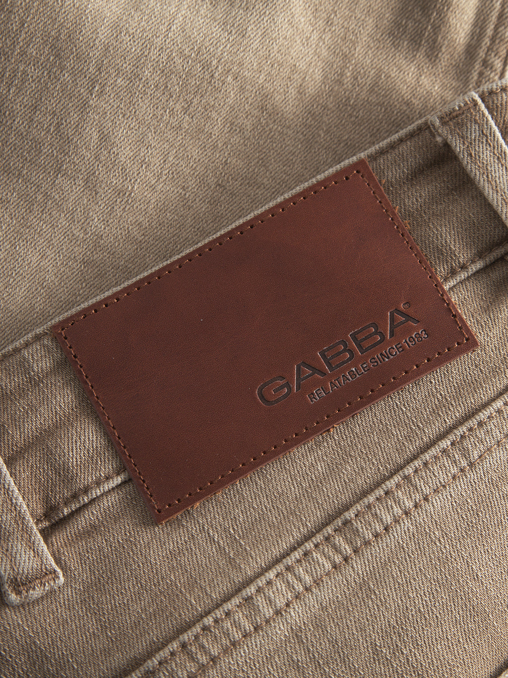 Close-up of GABalex Earth - Sand relaxed-fit jeans in sand-toned denim, featuring a brown leather waistband patch embossed with Gabba and 
