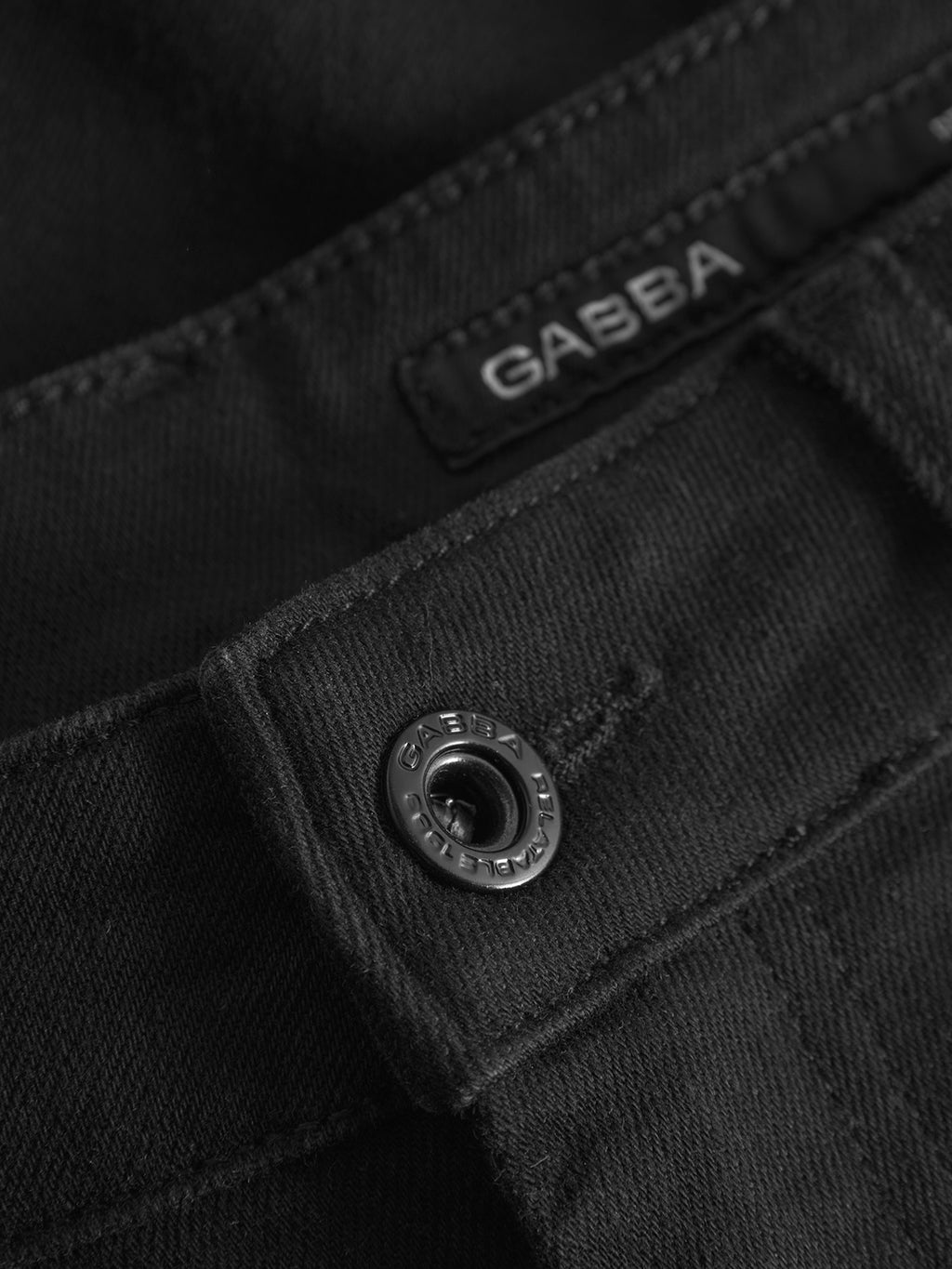 Close-up of GABmarc Sword - Black Denim jeans by Gabba, featuring intense black fabric, a metal Gabba-branded button, and a black label with the Gabba name stitched above the waistband for a sharp, clean look.