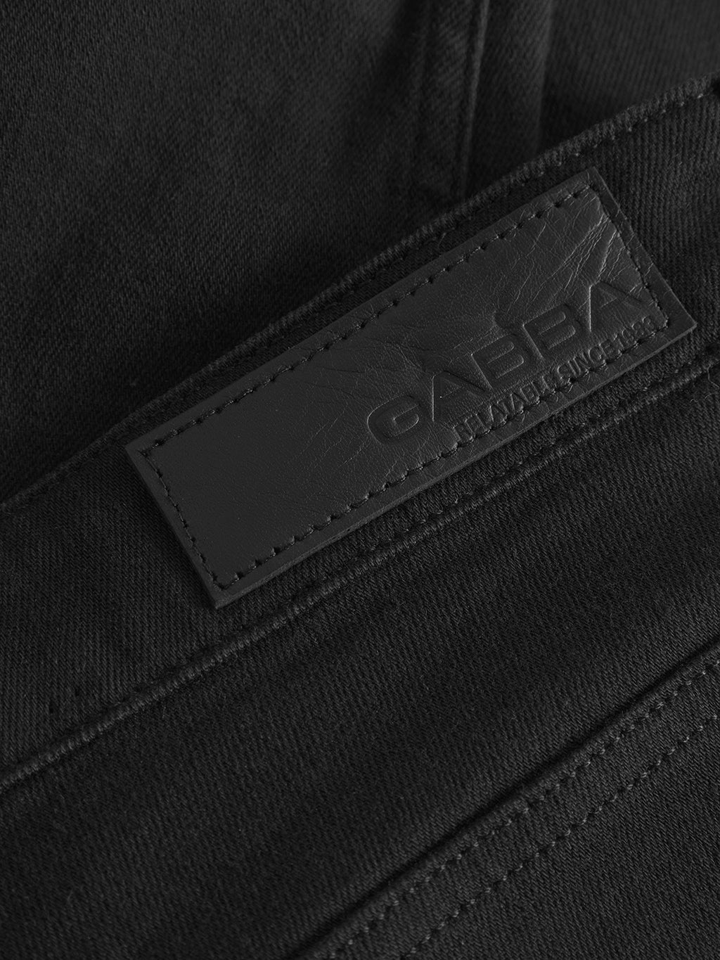 Close-up of a black leather patch embossed with Gabba and ESTABLISHED SINCE 1983 on GABmarc Sword - Black Denim jeans. Visible stitching and fabric texture highlight the slim fit's sharp, clean look.