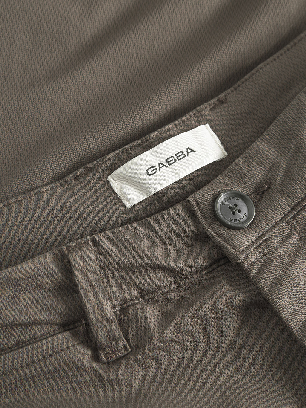 Close-up of GABpaul K3280 Dale Chino in dark brown by Gabba, featuring slim fit, French pockets, button waistband with belt loops, and white Gabba label sewn inside.