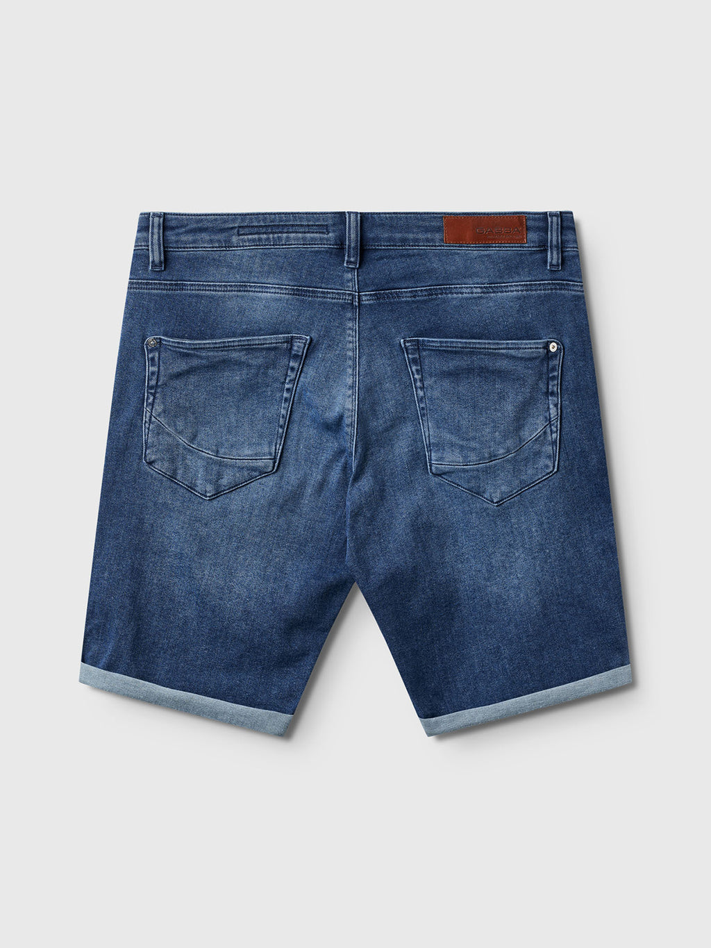 Back view of Gabba Jason K3787 SANZA Shorts in mid blue denim, featuring rolled hems, two back pockets, belt loops, and a brown leather patch on the waistband. Made from high-flexibility super-stretch fabric. Displayed on a plain background.