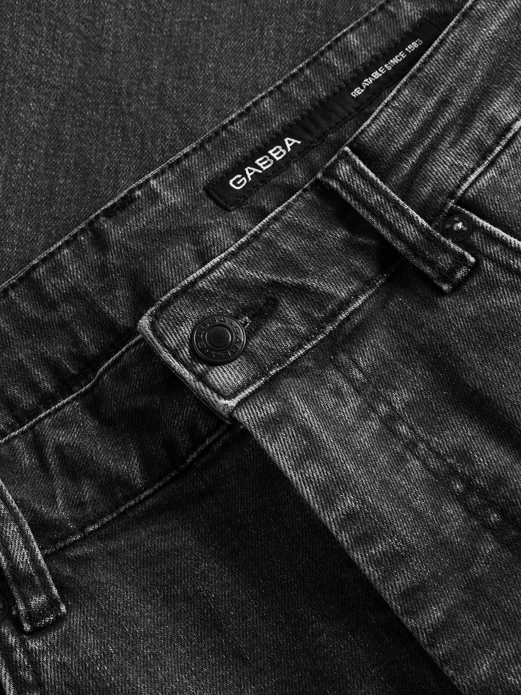 Close-up of the waistband and button on black regular fit Gabba GABmarc F1011 jeans, showing a sewn-in Gabba label. The denim fabric has a slightly faded texture.