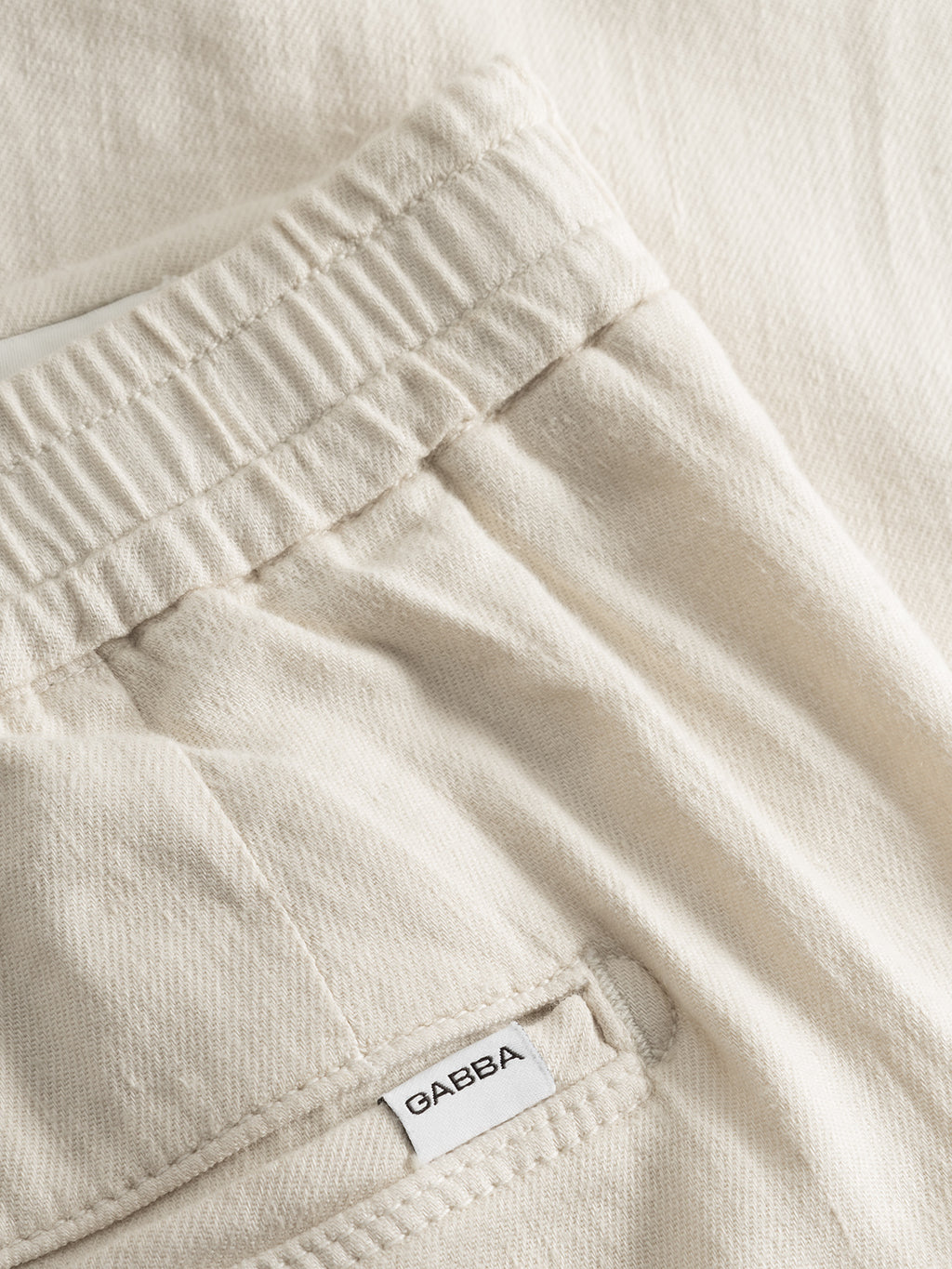 Close-up of Gabba Napoli 19 Twill Linen pants in Birch—a classic-fit style with an elastic waistband, visible back pocket featuring a white Gabba label, and soft textured fabric for all-day comfort.