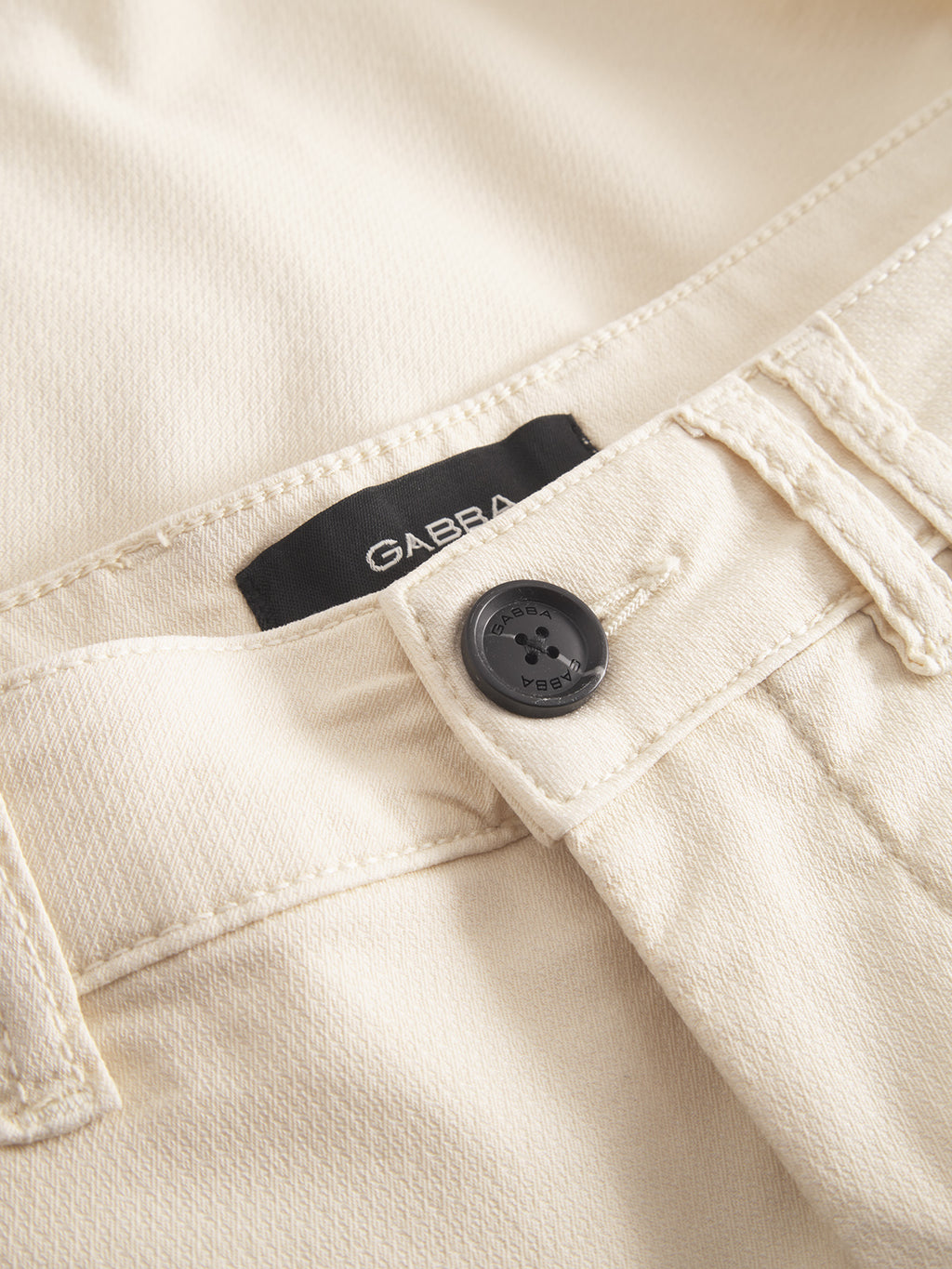 Close-up of Gabba GABjet K3280 Dale Shorts in Ecru Light, showing cream color, black button, visible belt loops, and a partially hidden black Gabba label under the waistband.