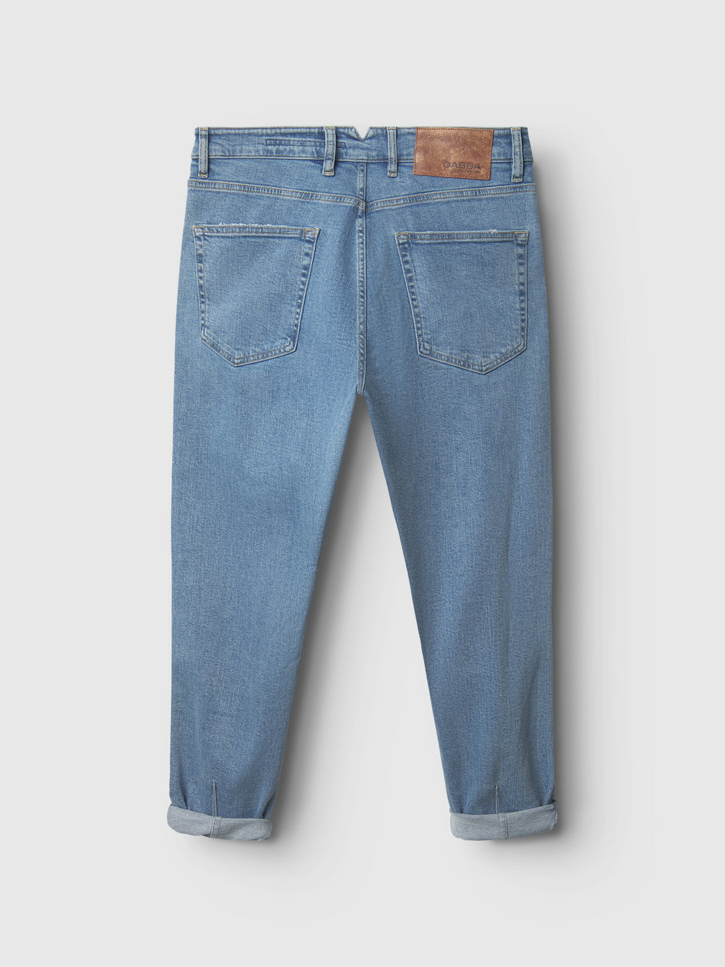 The Gabba GABalex Cross Lt. Blue Denim jeans feature two back pockets, rolled-up cuffs, belt loops, and a brown leather patch on the waistband, all in a light blue wash.