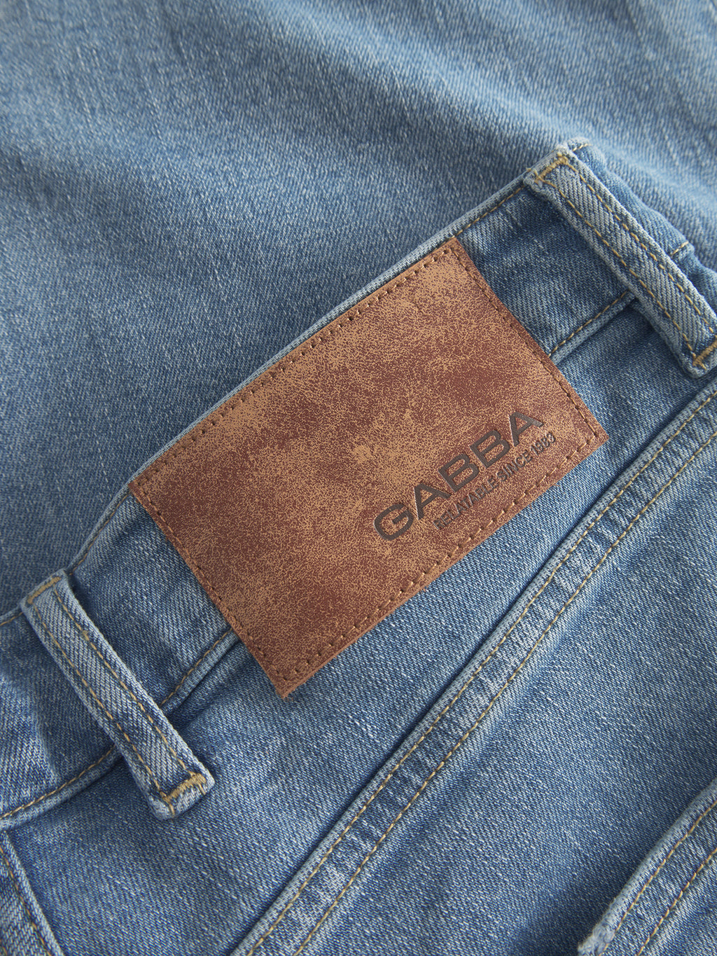 Close-up of GABalex Cross - Lt. Blue Denim jeans by Gabba, showing a brown leather patch with the brand name above the back pocket.