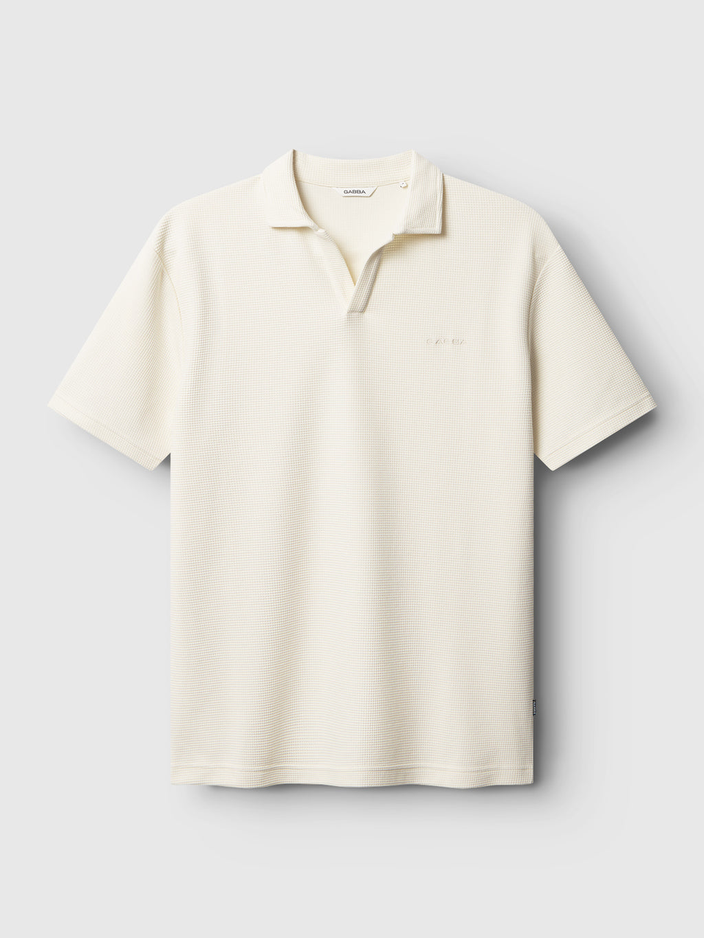 The Gabba GABlio Waff in Bone White is a cream-colored, short-sleeve polo with an open collar and relaxed fit. Made from midweight waffle fabric with subtle texture, it's shown against a plain light gray background.