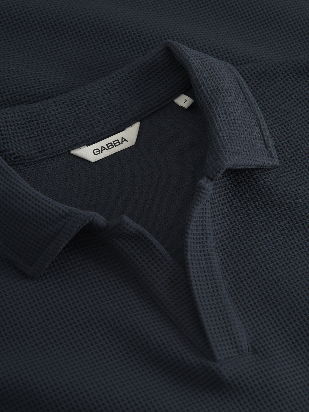 Close-up of the Gabba GABlio Waff in Navy, a dark textured polo shirt crafted in midweight waffle fabric. Features include an open collar, short placket, and internal white tag with “Gabba” inside the collar. No visible buttons.