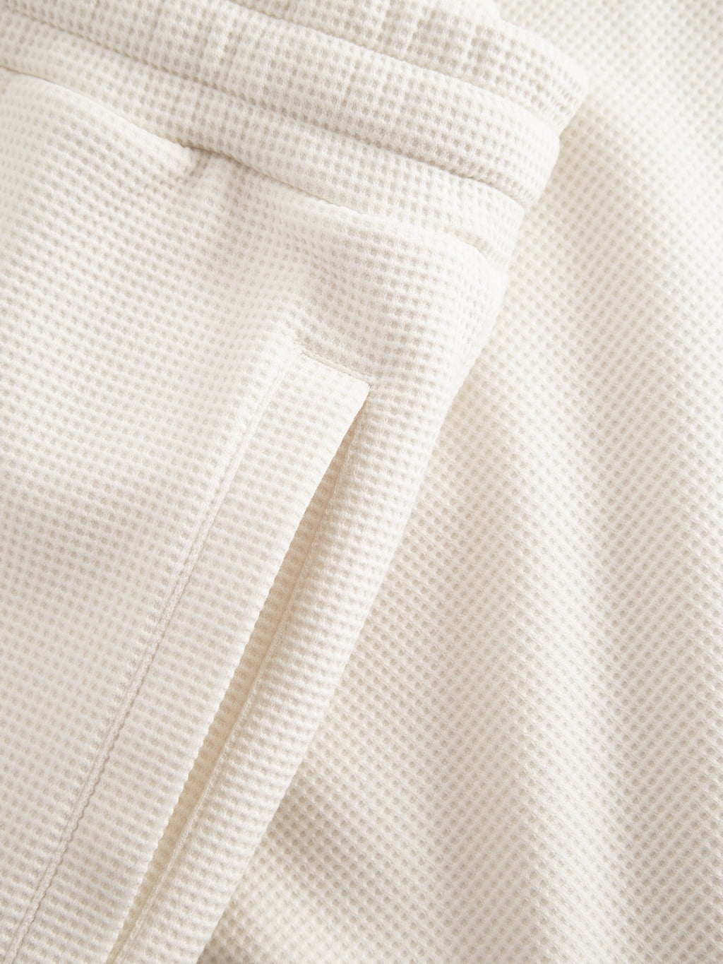 Close-up of Gabba's Tim Waff sweatpants in Bone White, featuring a cream waffle-knit fabric with a subtle square pattern, highlighting the waistband and pocket seam details.