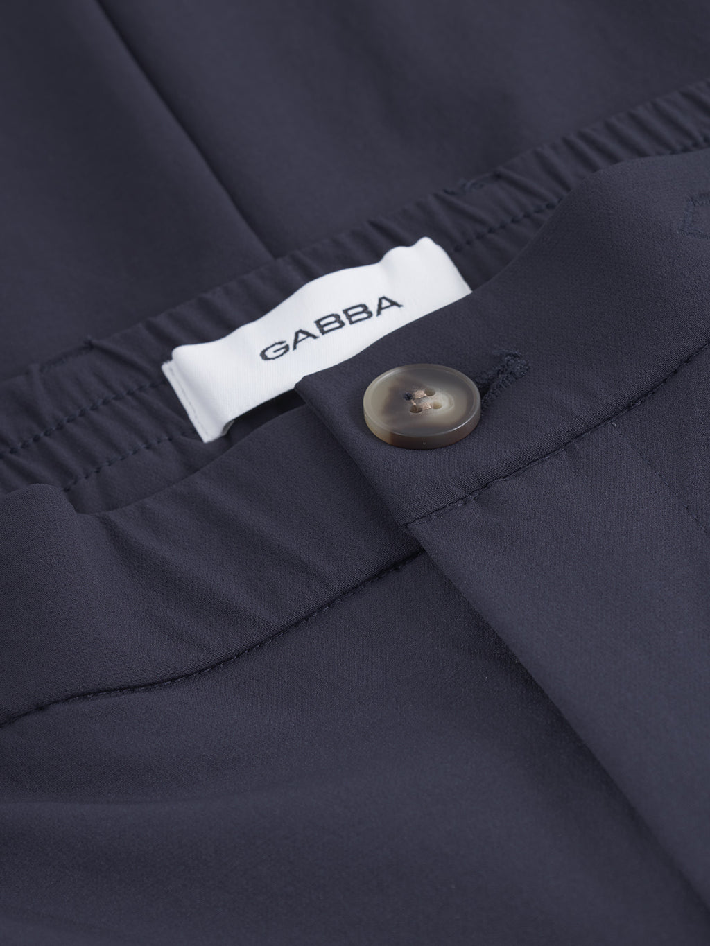 Close-up of Gabba GABmonza Tech pants in dark navy, featuring an elastic waist, relaxed straight fit, single brown button, and a white Gabba label above the waistband.