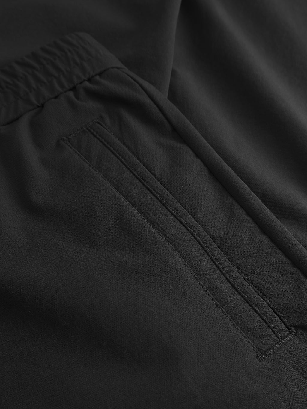 Close-up of Gabba's GABmonza Tech pants in black, with an elastic waist, relaxed straight fit, smooth matte tech fabric, and a neatly stitched horizontal welt pocket.
