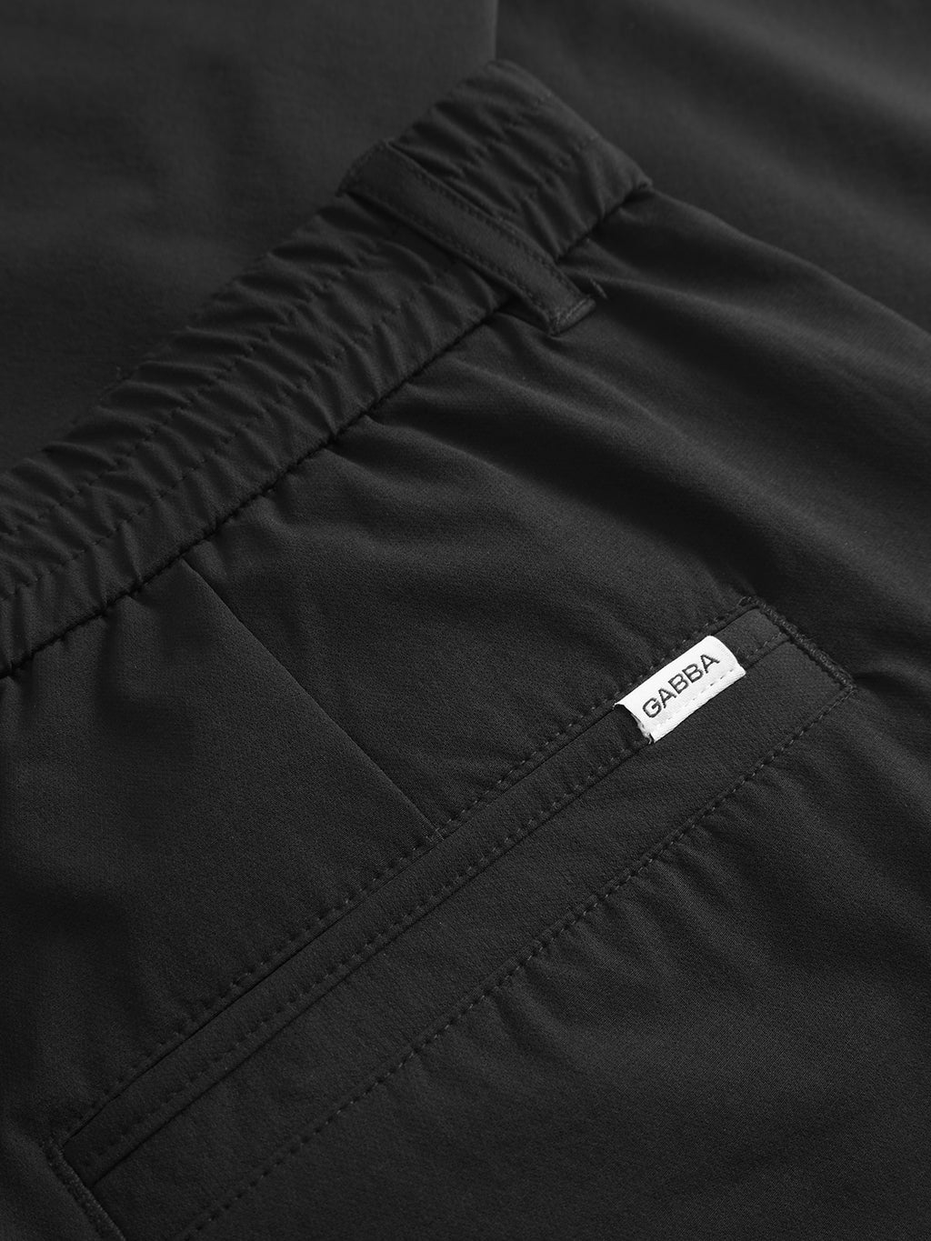 Close-up of Gabba GABmonza Tech - Black elastic waist pants with a relaxed straight fit, elastic waistband, back pocket, and a small white 