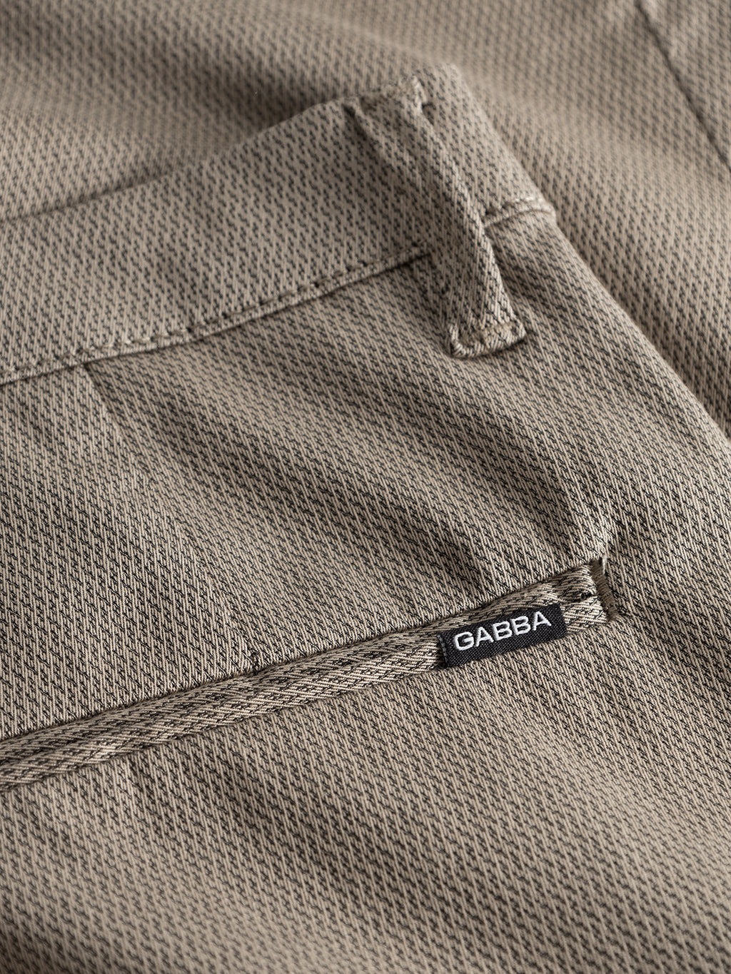 Close-up of a textured beige fabric pocket on GABBA Pisa K3280 Dale Pants - Humus, featuring high-stretch cotton-blend material and a small black GABBA label sewn near the seam.